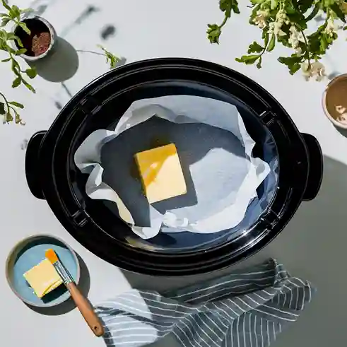 A slow cooker lined with parchment paper and a piece of butter placed in the center.