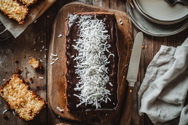 A freshly baked kefir sheet cake topped with chocolate glaze and shredded coconut on a rustic table.