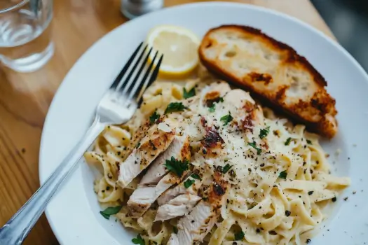 A plated dish of rotisserie chicken pasta garnished with parsley, Parmesan, and a side of garlic bread.