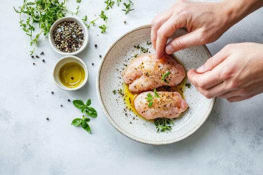 Hands seasoning boneless chicken breasts with sea salt and pepper, preparing it for the carob dipping process.