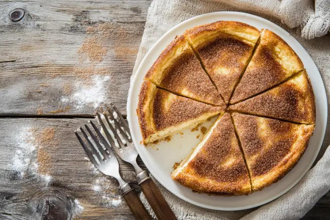 Overhead view of churro cheesecake squares with a golden cinnamon sugar topping on a white plate.