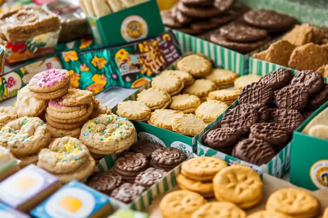 Colorful assortment of Girl Scout cookies, including Samoas, Thin Mints, and Trefoils, arranged on a rustic wooden table.